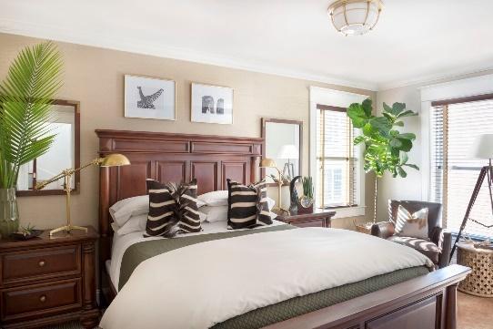 An image of a bedroom with a dark wood bed and 2 night stands showing potted plants in corners.