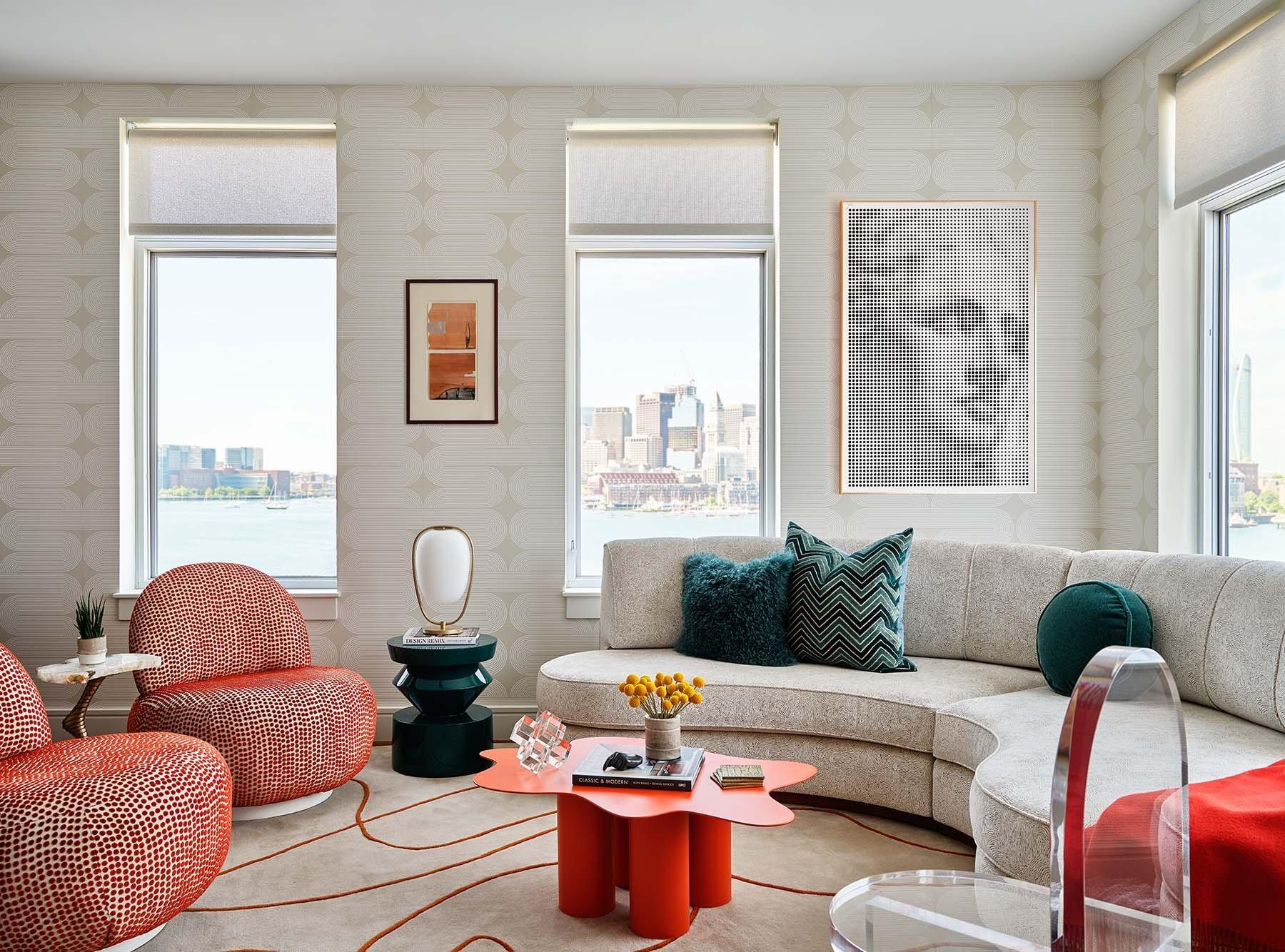 An image of Trevor Fulmer Design Vibrant Flair showing an off white semi circle sofa with green toss pillows and side table and an orange coffee table and 2 round chairs with a city in the background.
