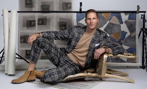 An image of Trevor Fulmer lounging on the floor with hanging color swatches and rugs in the background.