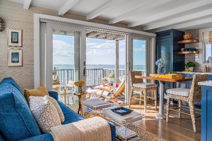 An image of the living room, dining room and kitchen of their seaside condo with French doors to the outdoor deck showing Westminster Teak Captain Steamer and an ocean view.
