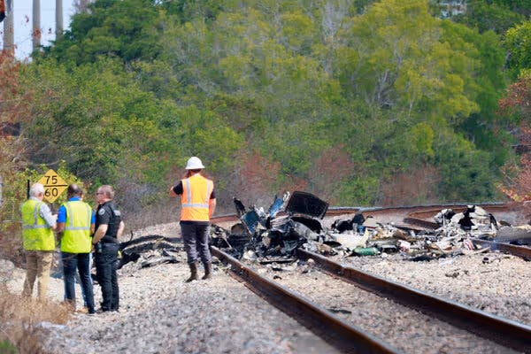 Emergency workers standing near debris from a small plane crash on a set of train tracks.