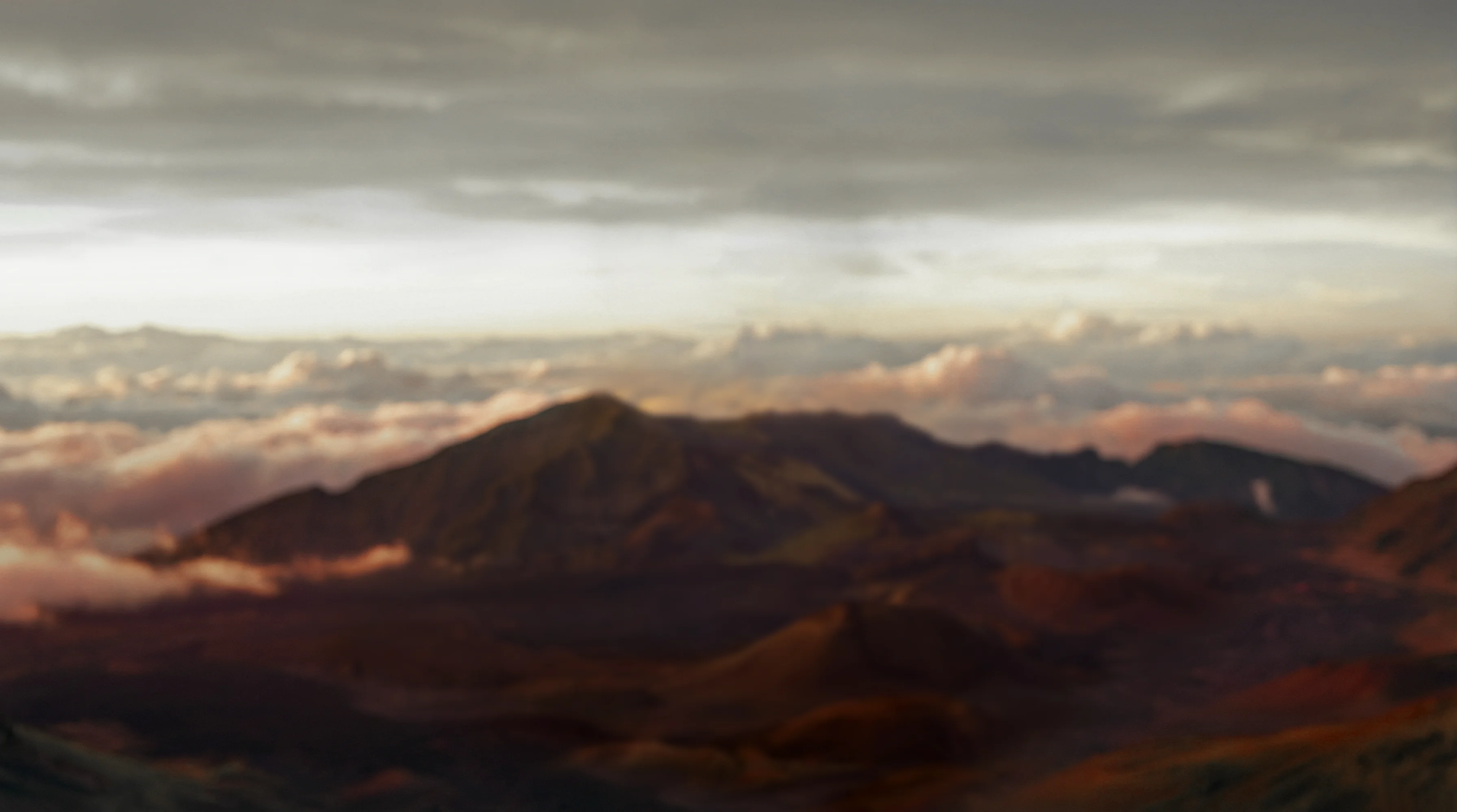 Blurry landscape of mountains under a cloudy sky with soft light on scattered clouds.