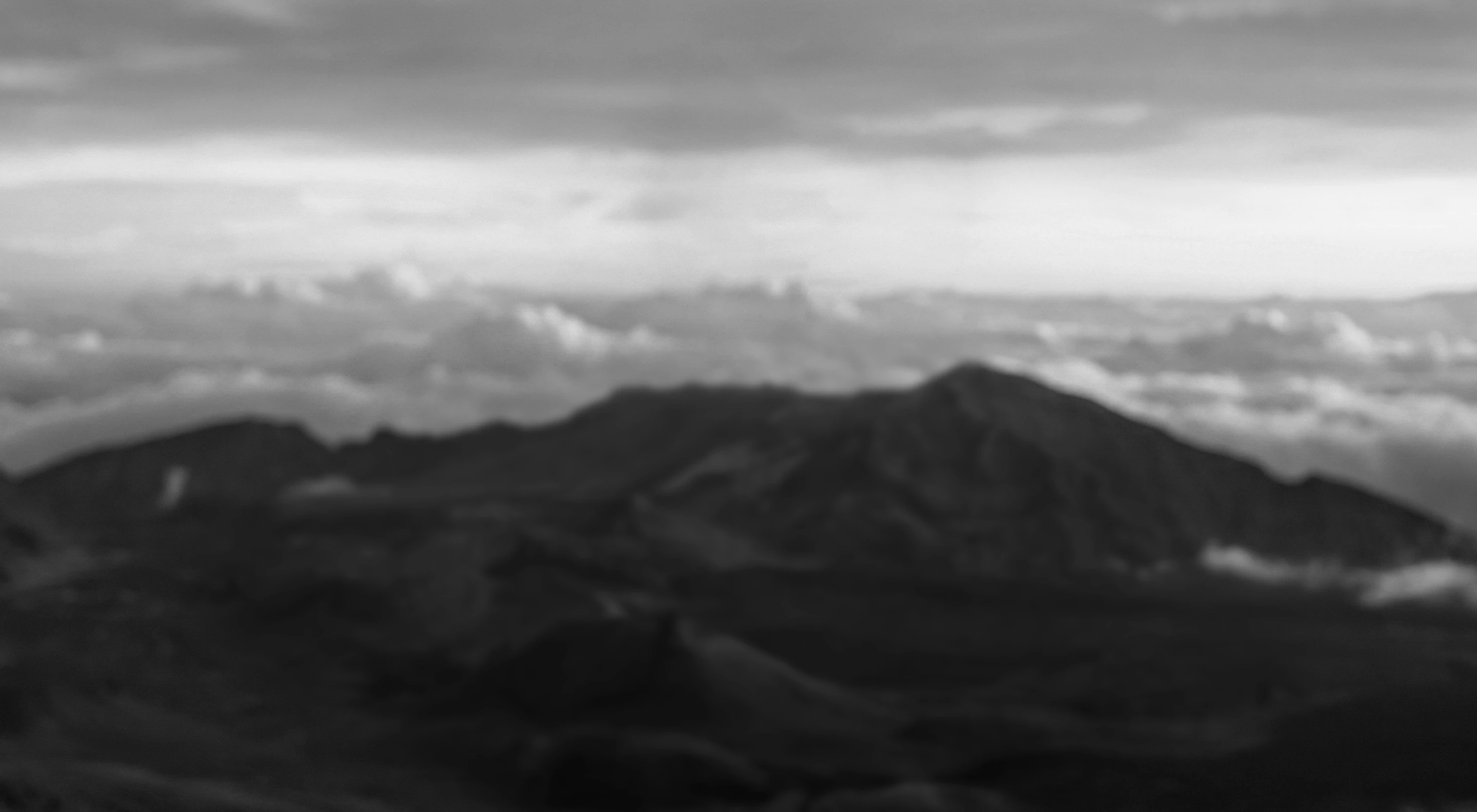 Blurry black and white image of mountains with clouds in the background.