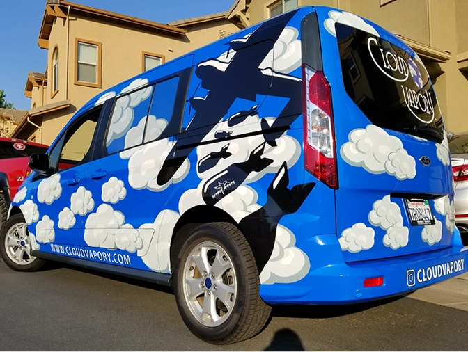 Blue van with a mural of white clouds and black airplane silhouettes, displaying the website www.cloudvapory.com and the Instagram handle @cloudvapory.
