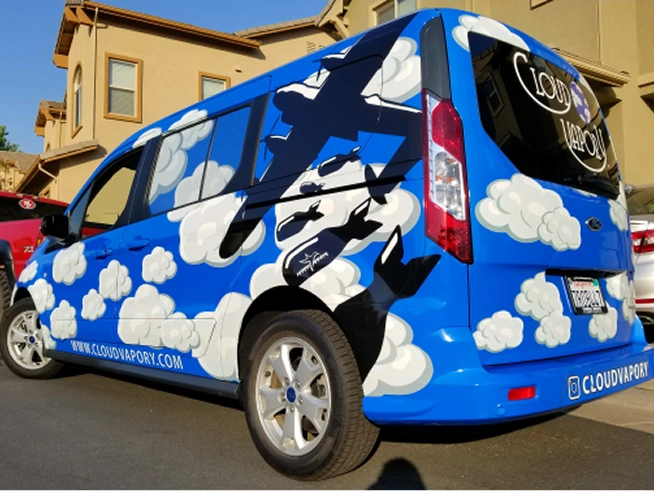Blue van with white clouds and black airplane silhouettes painted on its sides and rear, parked on a residential street.