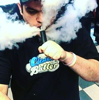 Person wearing a Cloud Batter shirt exhaling a large cloud of vapor from an electronic cigarette.