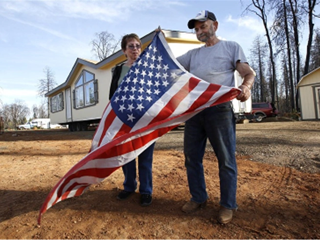 Two people standing outdoors holding and examining a large American flag.