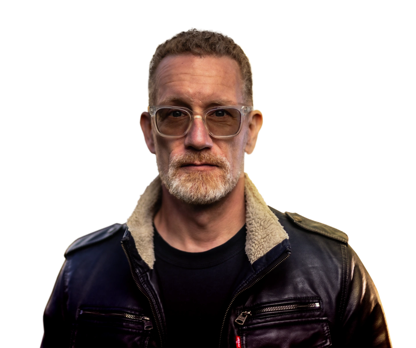 Middle-aged man with light beard and short curly hair wearing tinted glasses and a black leather jacket with a shearling collar.