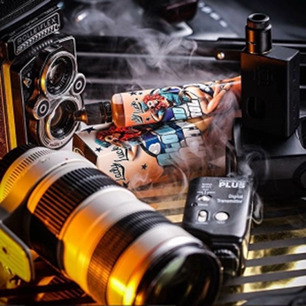 Vintage Rolleiflex camera, modern camera lens, vape device with colorful artistic packaging, and a wireless digital transmitter on a reflective surface with smoke.