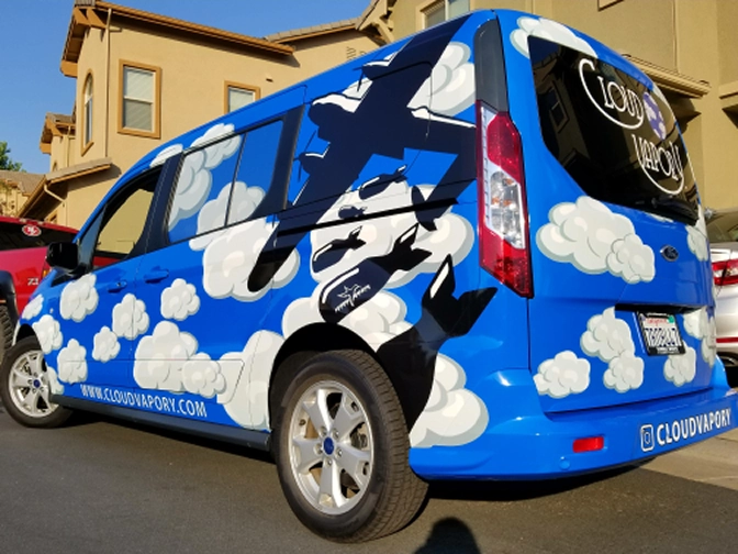 Blue van decorated with white cloud patterns and black airplane silhouettes parked in a residential area.