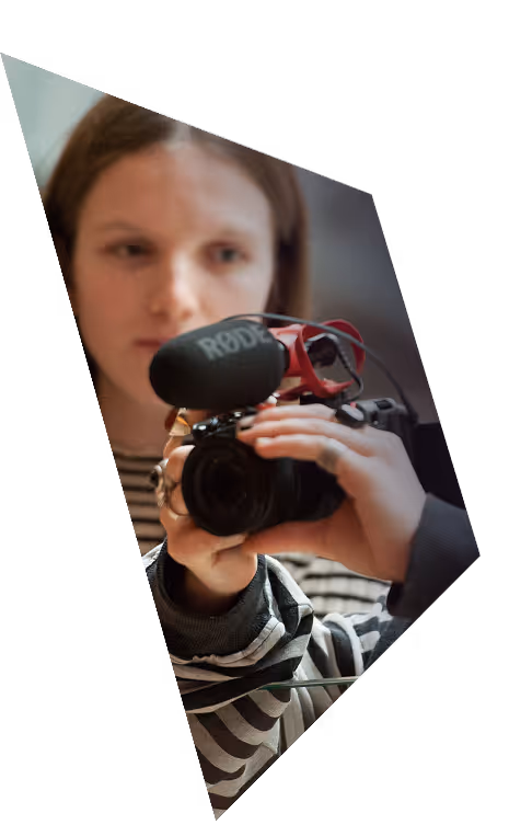 Person holding a camera with a Rode microphone attached, wearing a striped shirt.