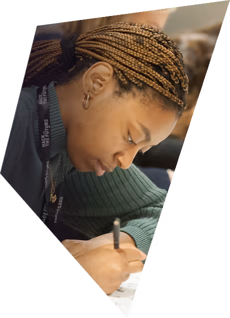 Woman with braided hair wearing a green sweater concentrating while writing with a pen.
