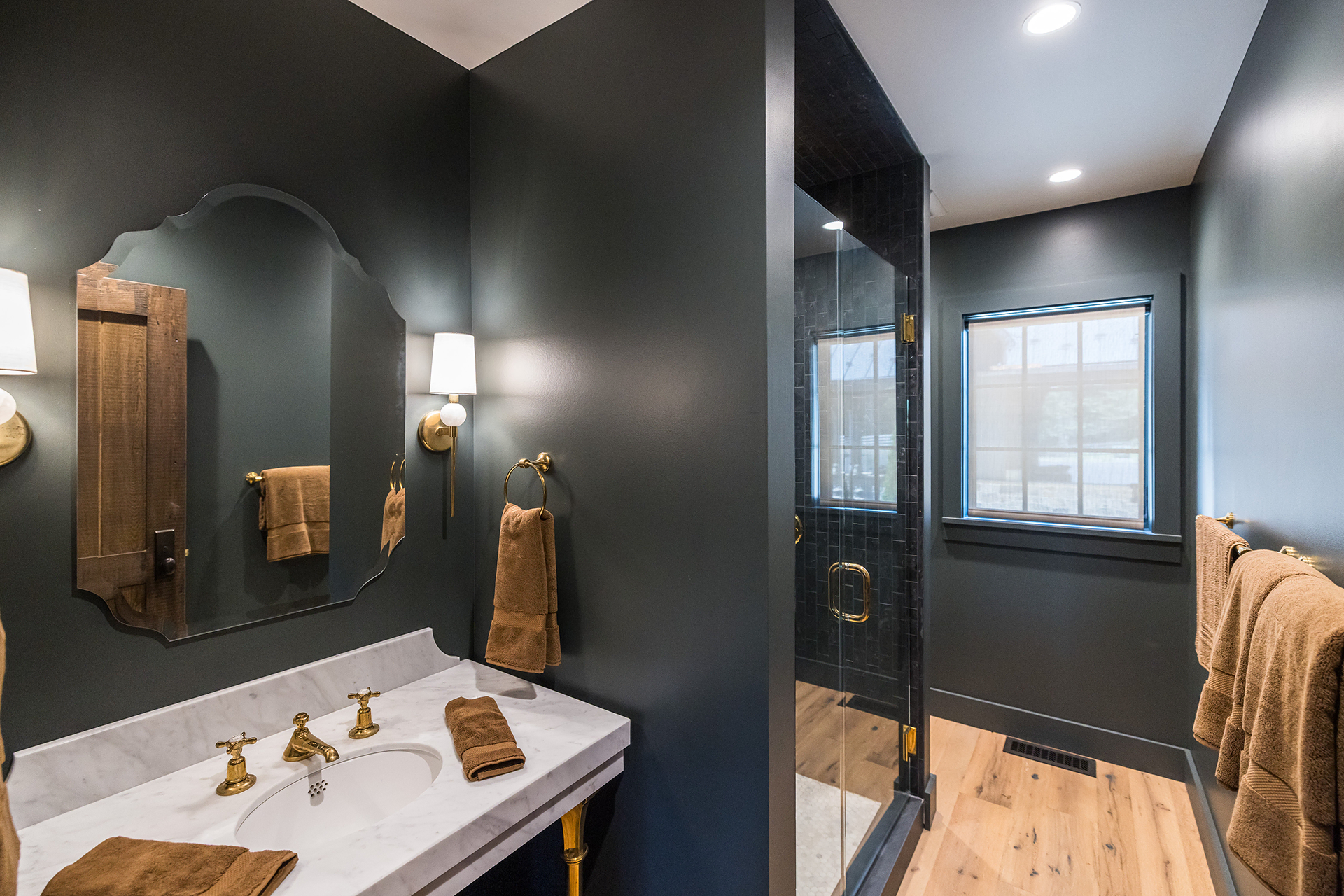 Bathroom in a barn apartment featuring dark walls, an ornate mirror, brass hardware, and white oak floors throughout.