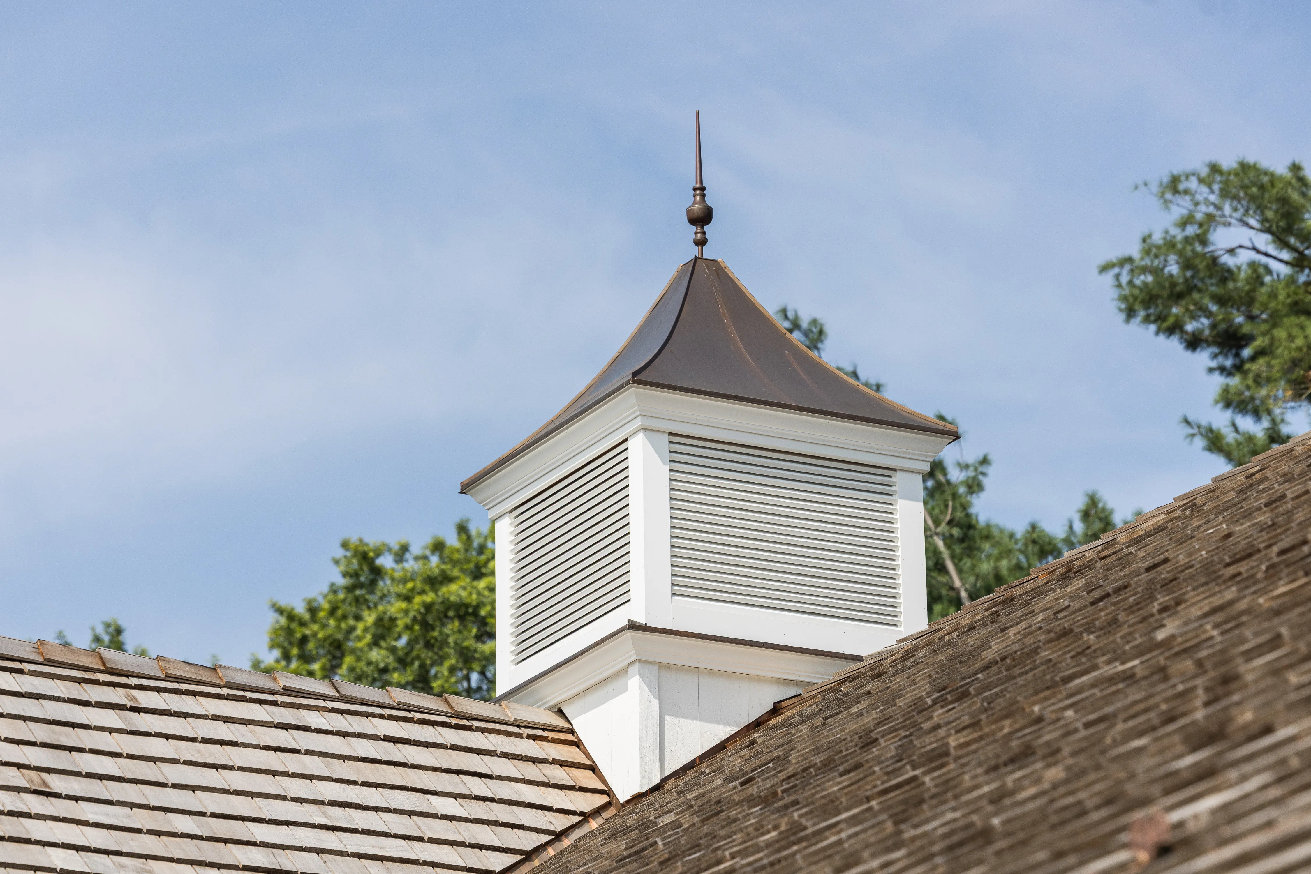 A close-up image of a custom wood cupola with a copper roof, surrounded by cedar shake roof shingles.
