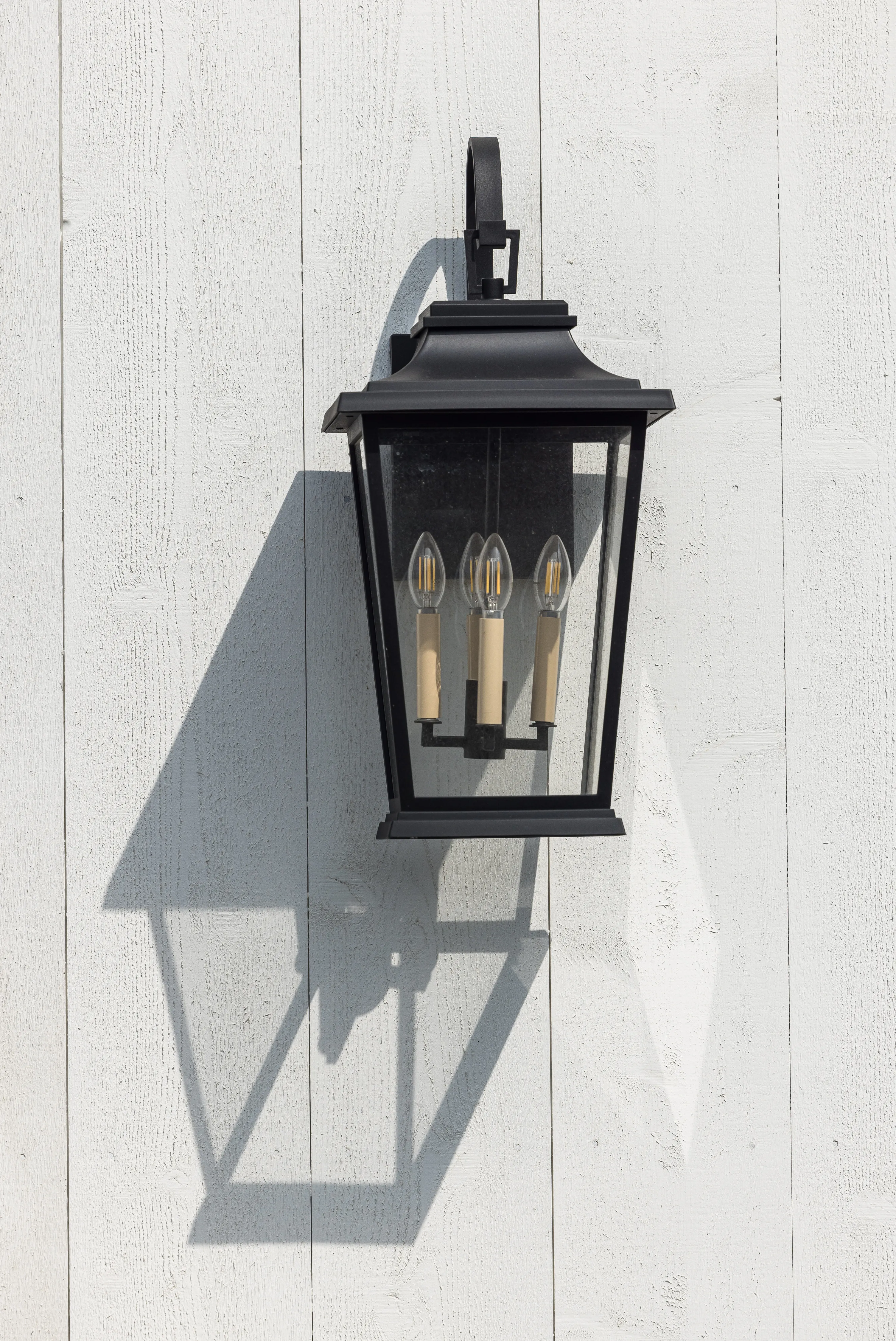 A close-up image of a black, lantern-style sconce framed beautifully by the white exterior wood siding.