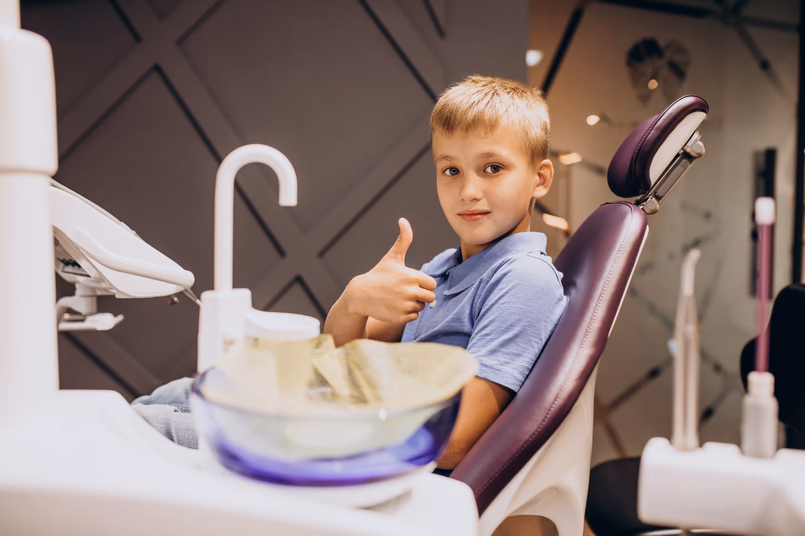 Boy sitting in a dental chair giving a thumbs-up gesture.