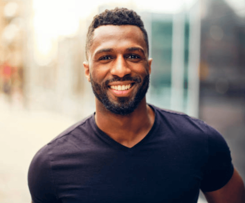 Smiling man with short curly hair and beard wearing a black t-shirt outdoors.