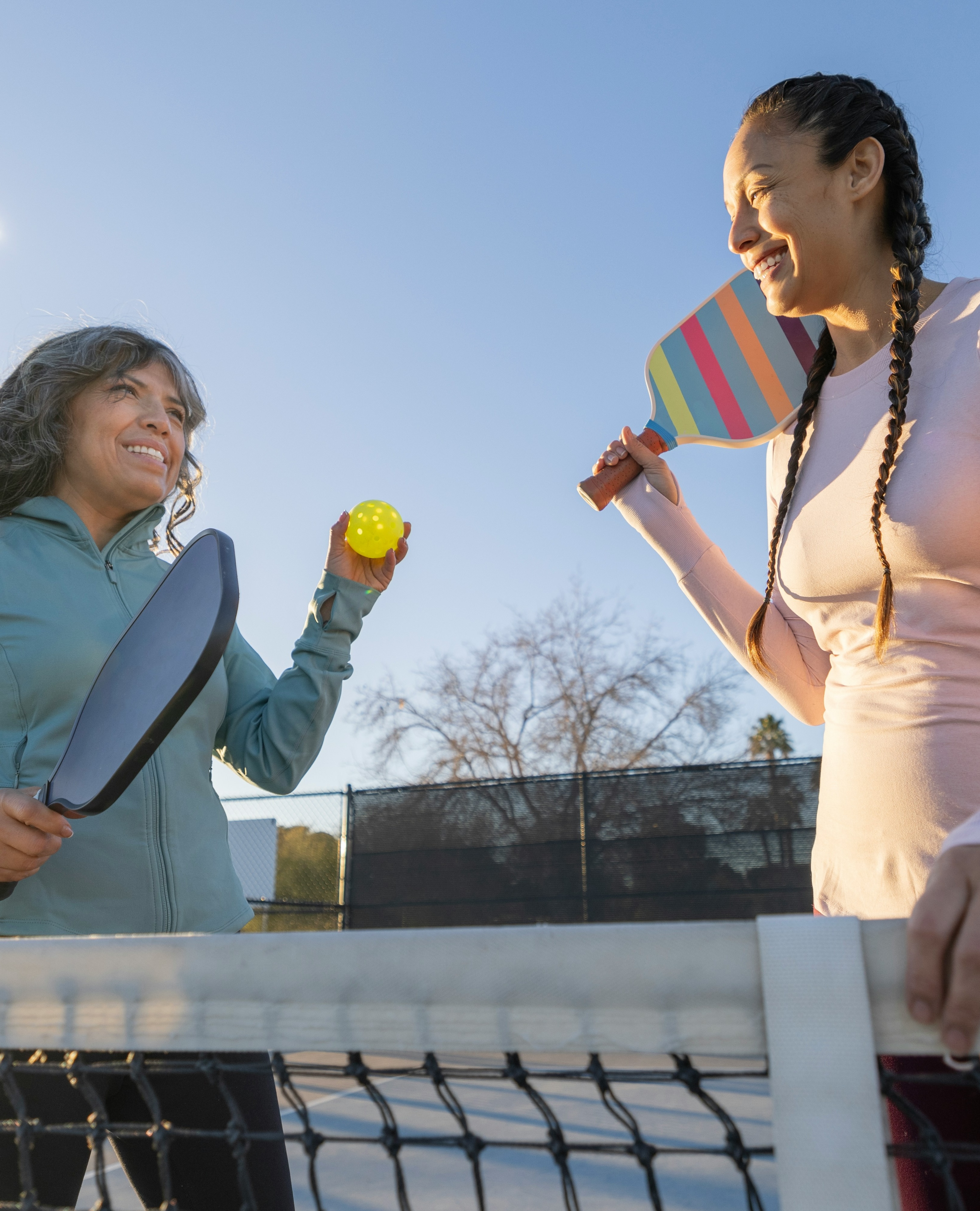 Two friends laughing on a pickleball court