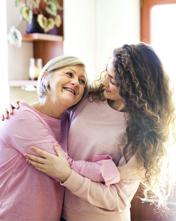 A mother and her grown daughter sharing a hug at home