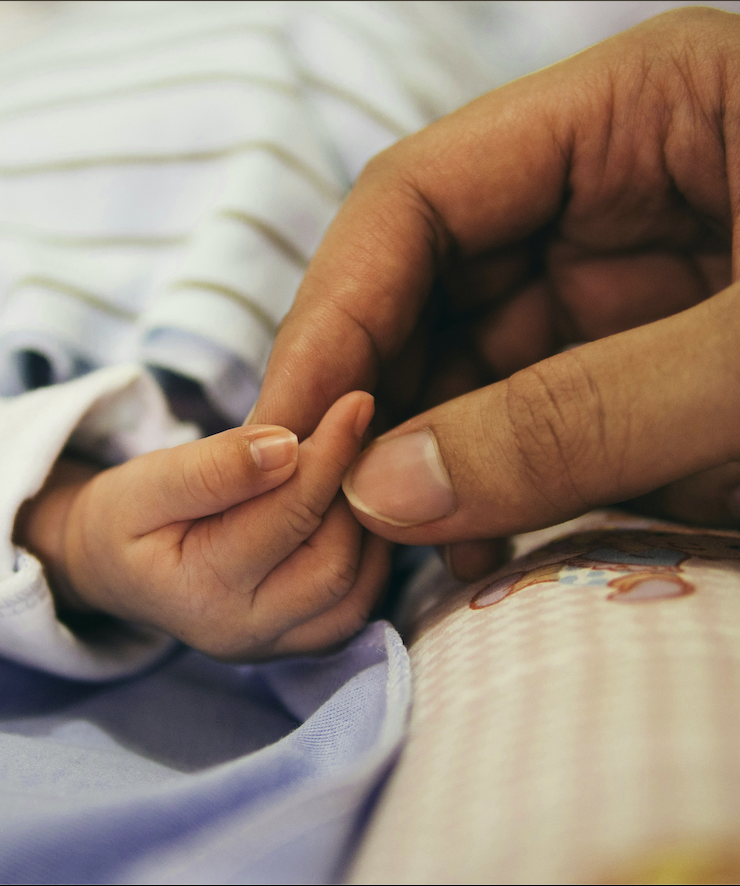 An adult hand gently holding a newborn's tiny fingers