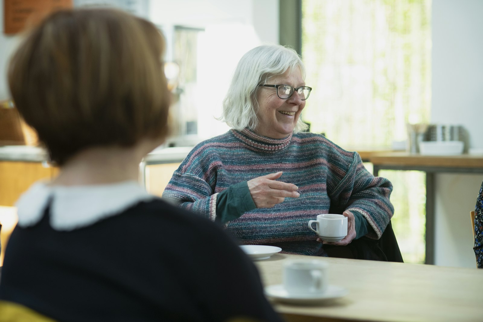 An older woman with silver hair talking with a younger woman over coffee
