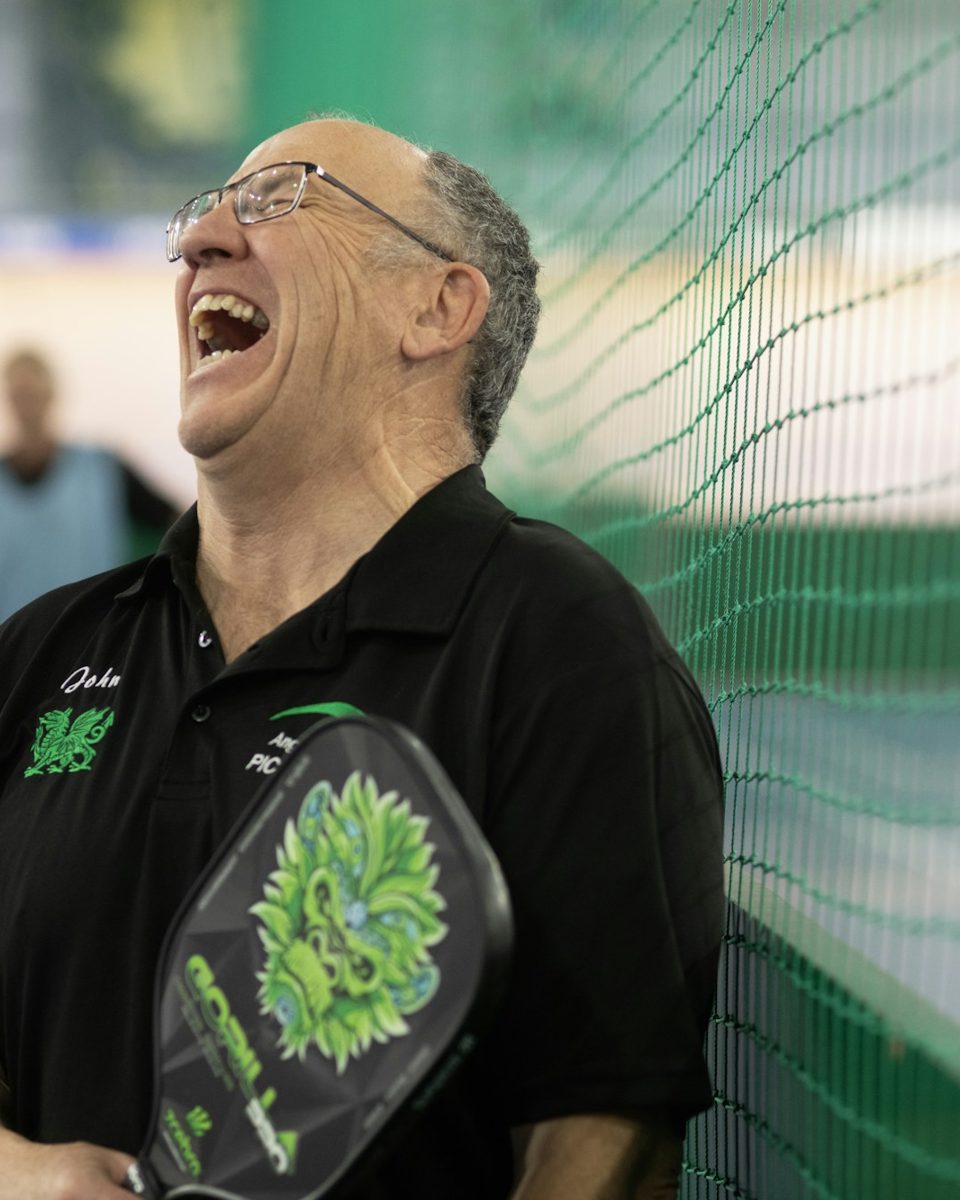 A man laughing with a pickleball paddle at an indoor court