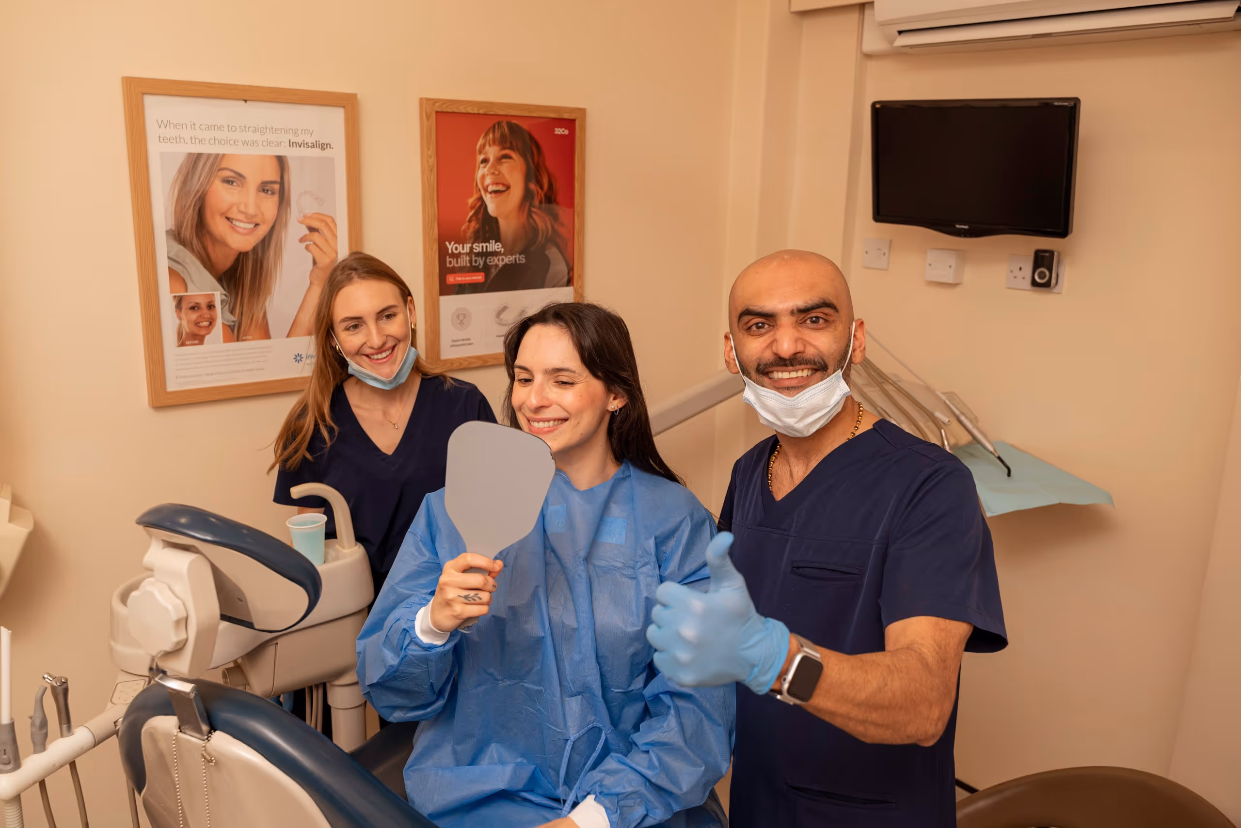 Smiling dental patient holding mirror with two dental professionals, one giving thumbs up in clinic.
