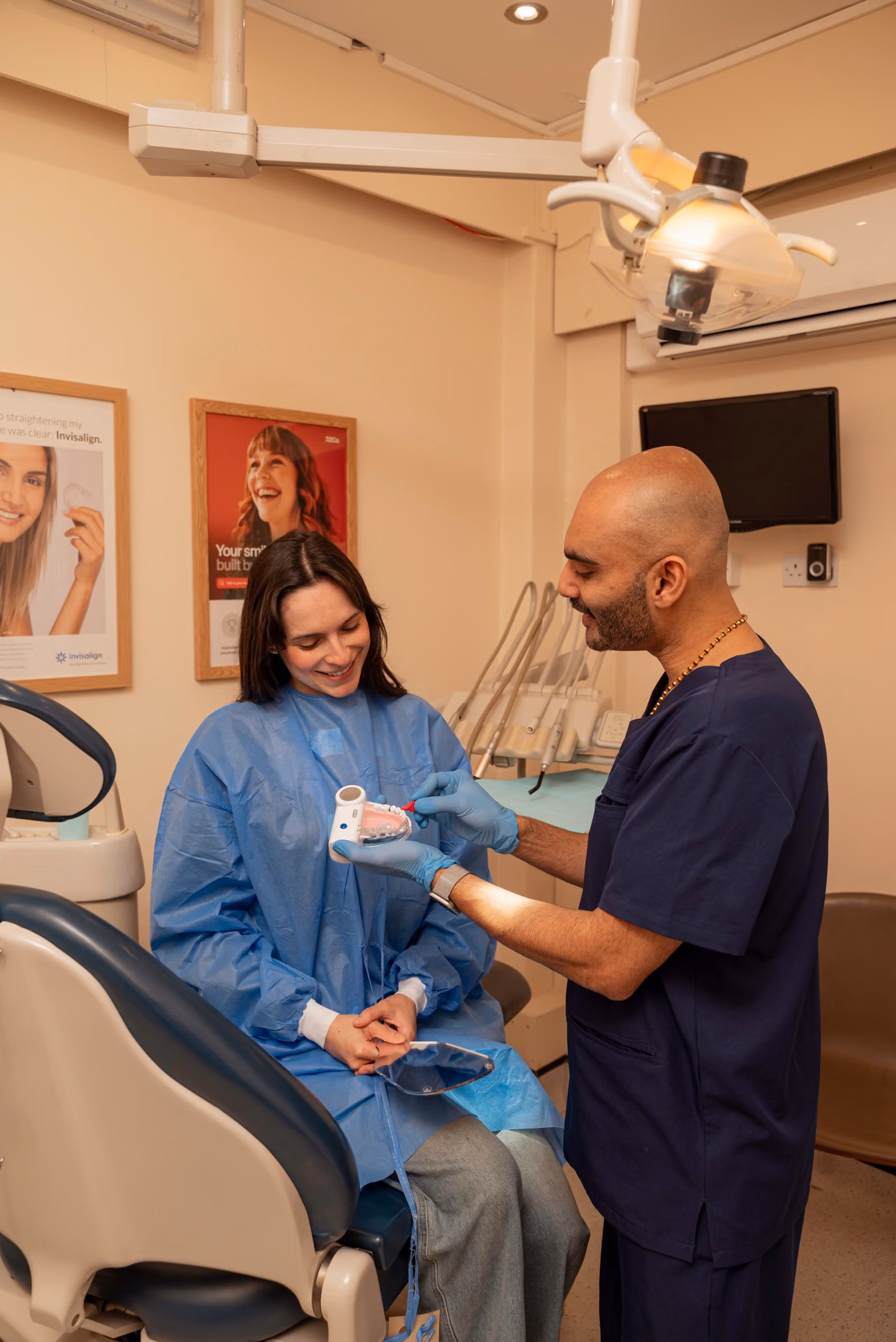 Dentist showing a dental model to a female patient wearing a blue protective gown in a clinic.