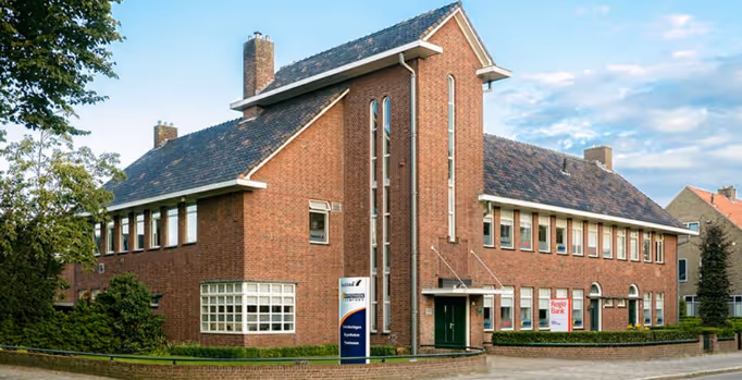 Groot rood bakstenen kantoorgebouw met meerdere ramen en een groene ingang in een rustige buurt.