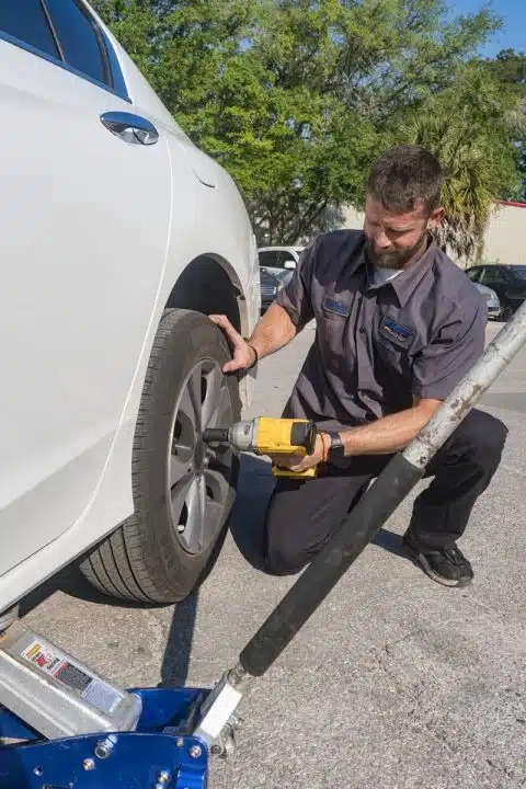 Elite Towing and Recovery technician changing a flat tire during a roadside assistance call in Gainesville, FL