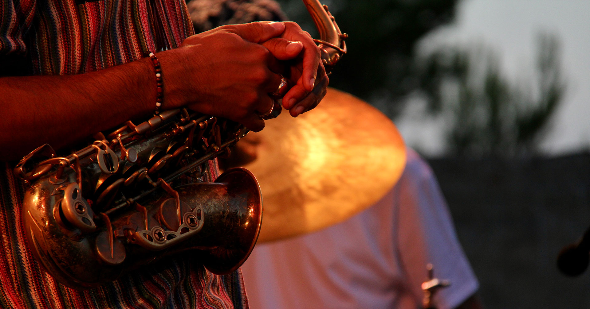 Mains d'un musicien tenant un saxophone avec un cymbale de batterie floue en arrière-plan.