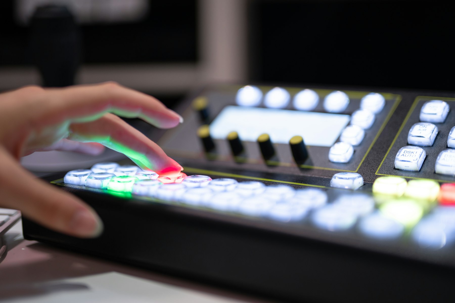 Hand pressing buttons on a lit broadcast vision switcher