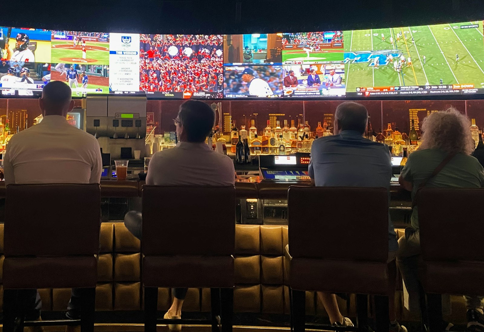 Viewers in front of a wide wall of screens showing multiple live sports feeds