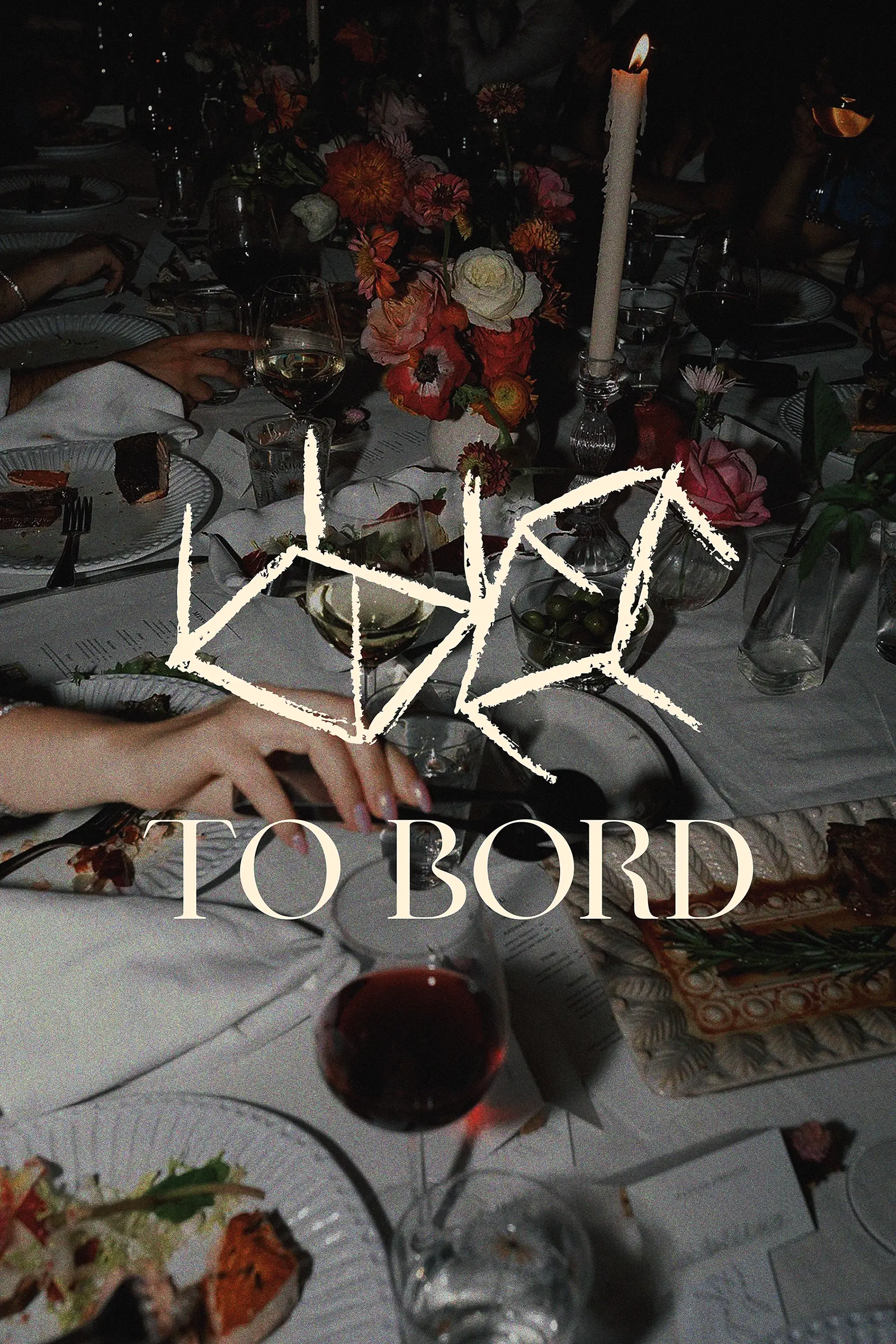 Dimly lit dining table with plates of food, wine glasses, a lit candle, and a flower arrangement, overlaid with stylized text 'TO BORD'.