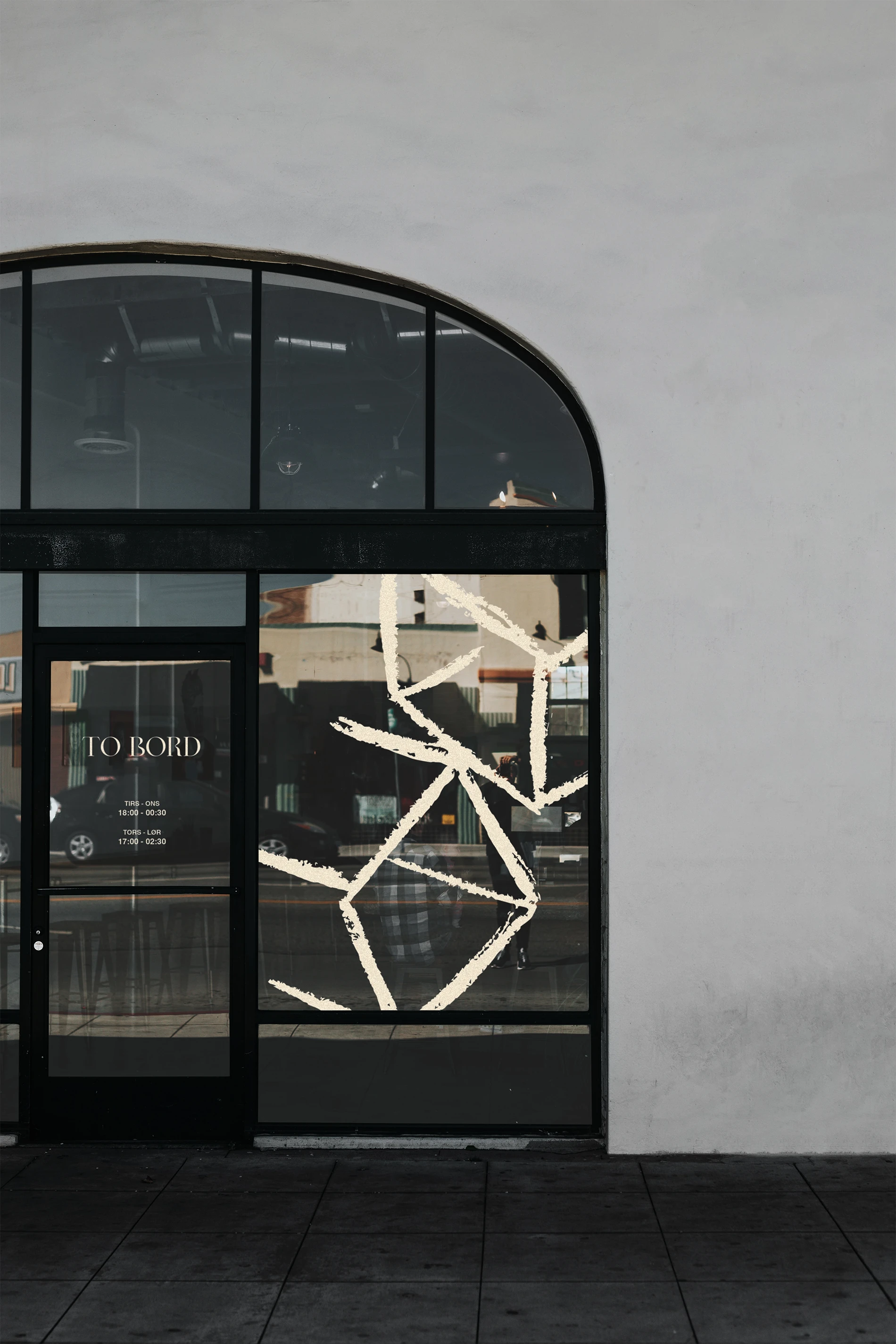 Black-framed glass door and window with abstract white geometric designs and business hours displayed on the door.