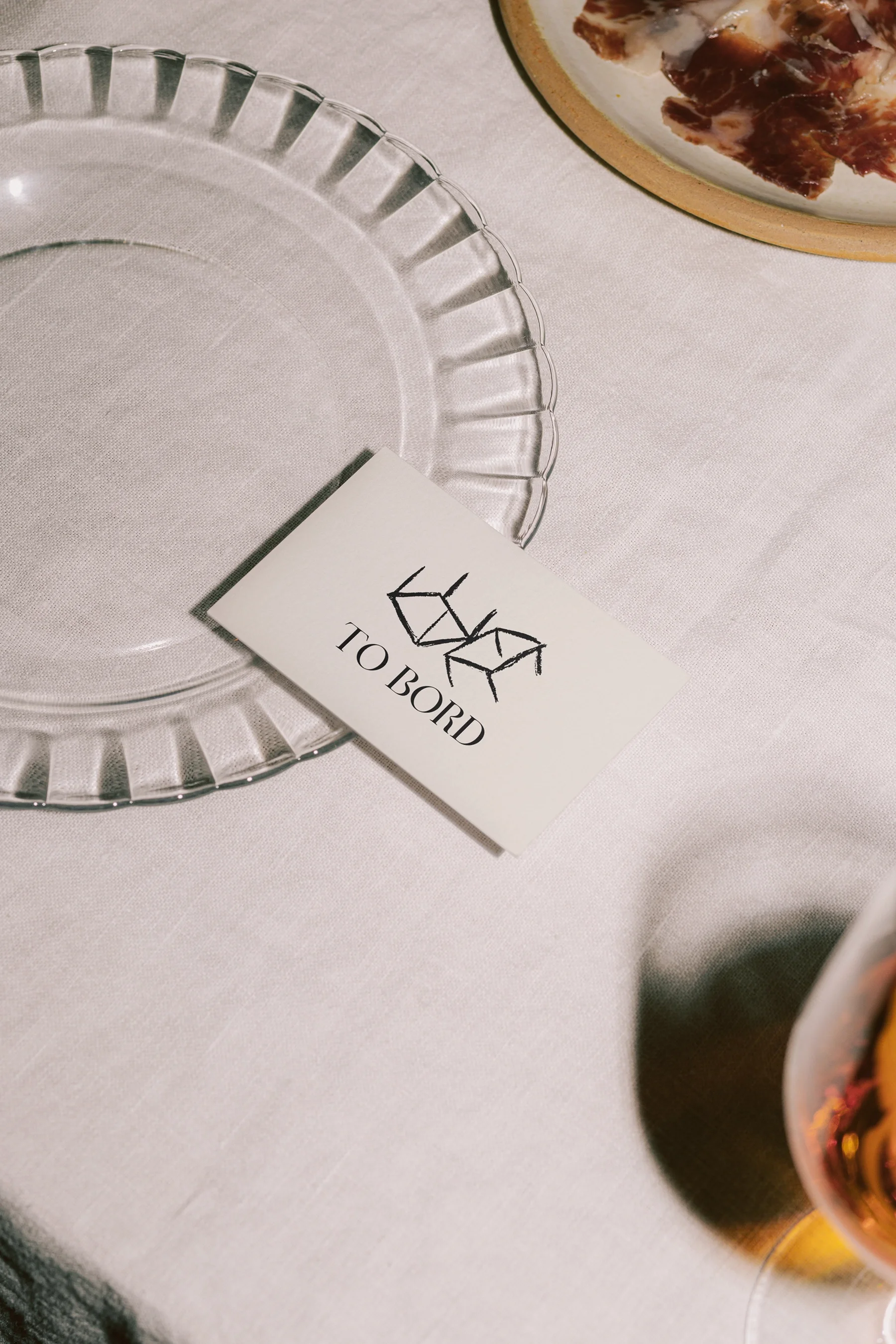 White napkin on table holding an empty glass plate and a card with two overlapping chairs and the text 'TO BORD'.