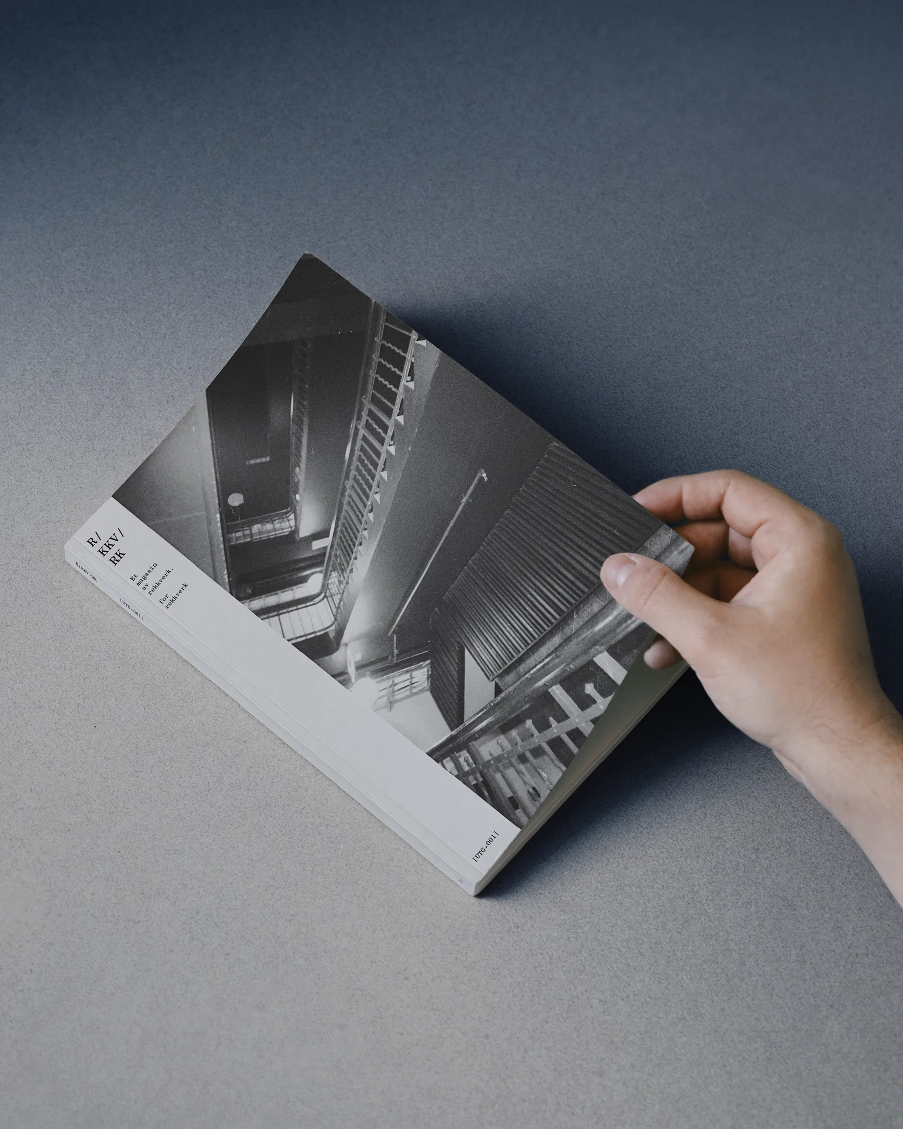 Hand holding a black and white book showing a photo of an upward spiral staircase.
