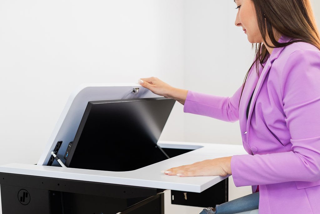 Person versenkt den Monitor im SMESK-Tisch und wandelt den Computertisch in Sekunden in eine freie Arbeitsfläche um