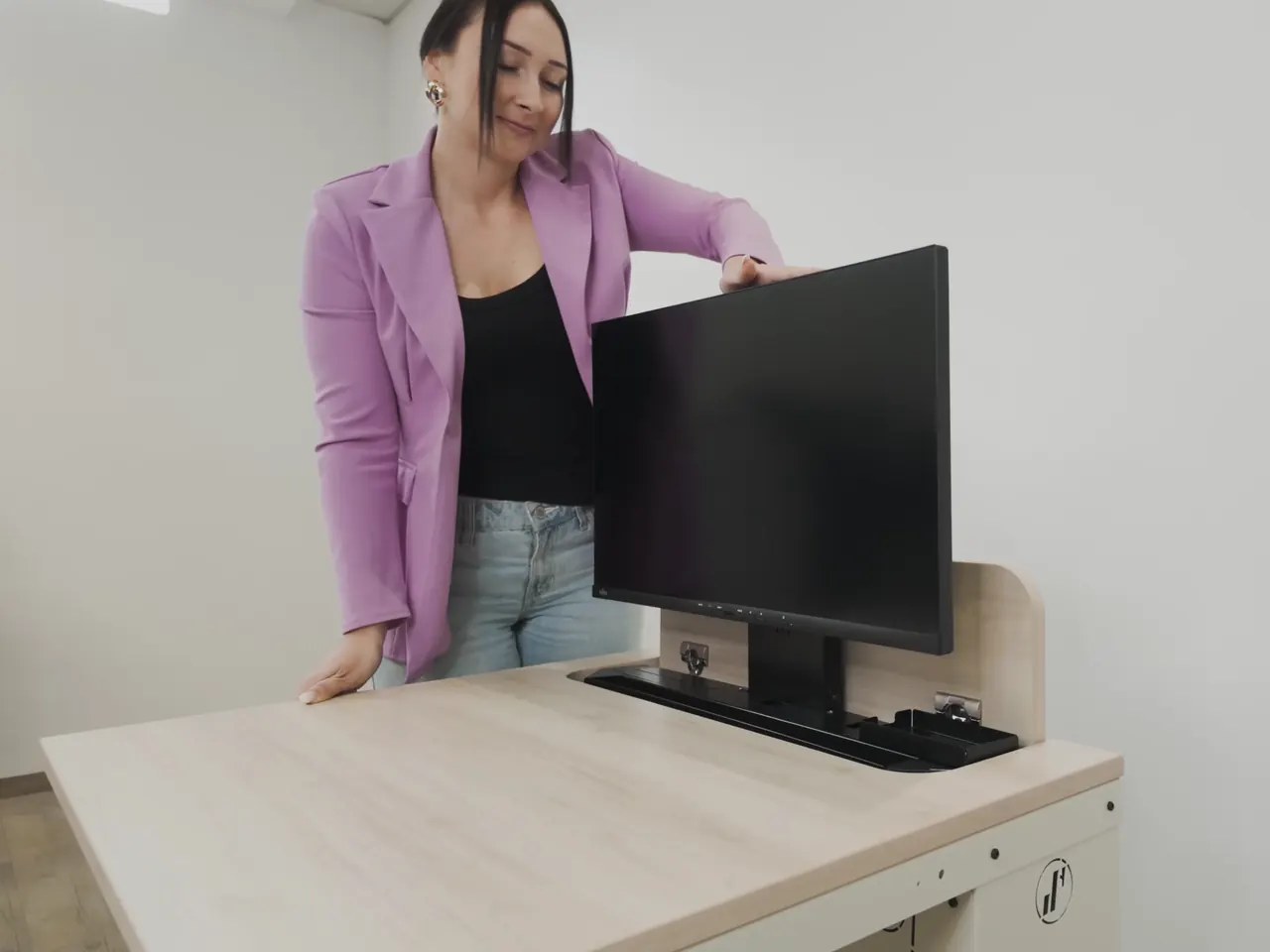 Eine Frau drückt den Monitor eines SMESK Lift in die Tischplatte, die Klappe schließt sich, danach fährt der Monitor wieder aus