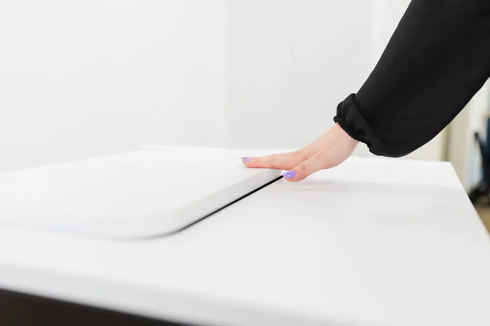 Eine Hand drückt die Klappe eines SMESK Flip flach in die weiße Tischplatte, am Rand bleibt eine schmale Fuge