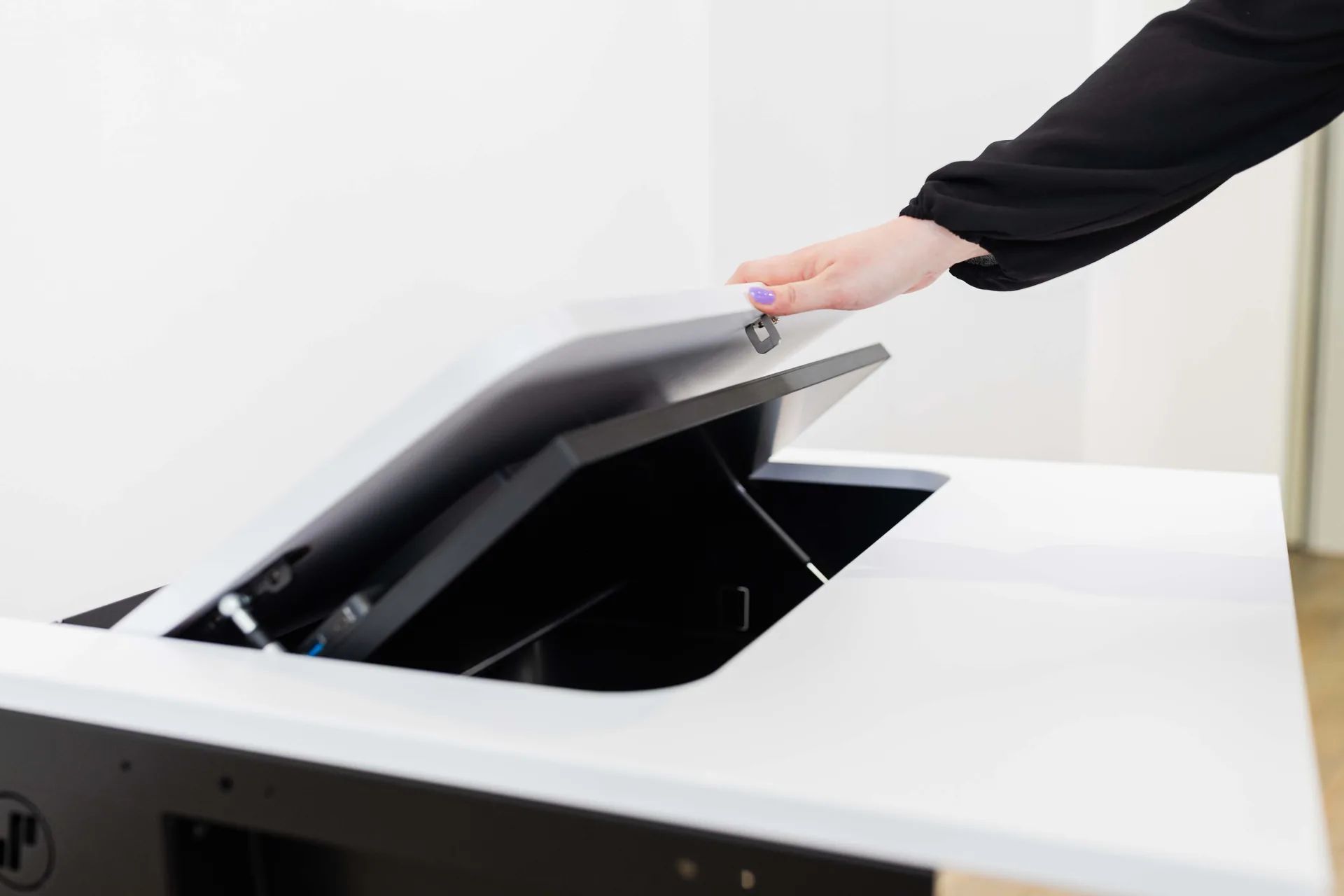 Eine Hand hält die aufgeklappte Klappe eines SMESK Flip, an der der Monitor sitzt, über dem Ausschnitt der weißen Tischplatte