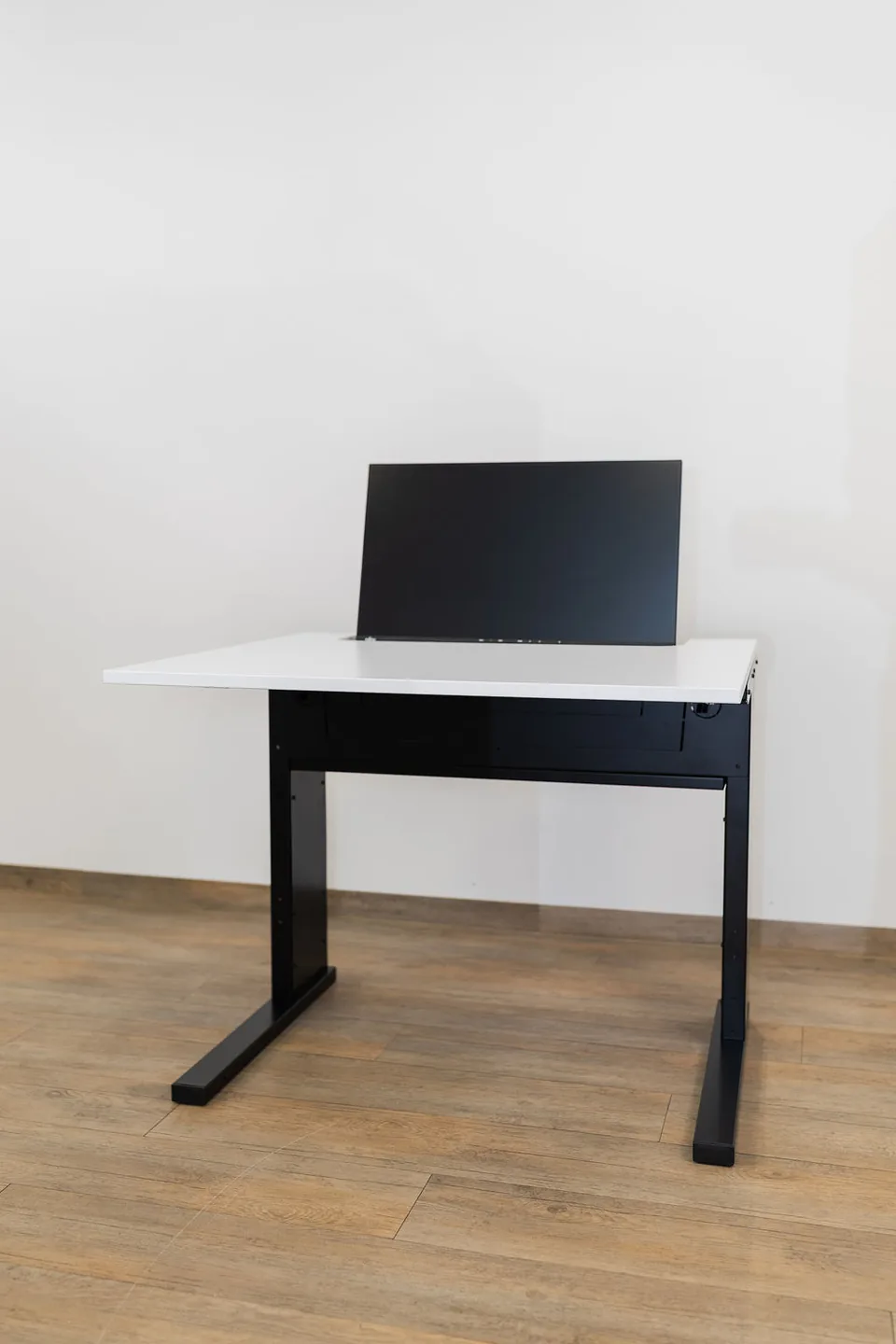 SMESK Semi Einzeltisch von vorn: der Monitor steht halb in der weißen Tischplatte, darunter das schwarze Gestell mit C-Füßen