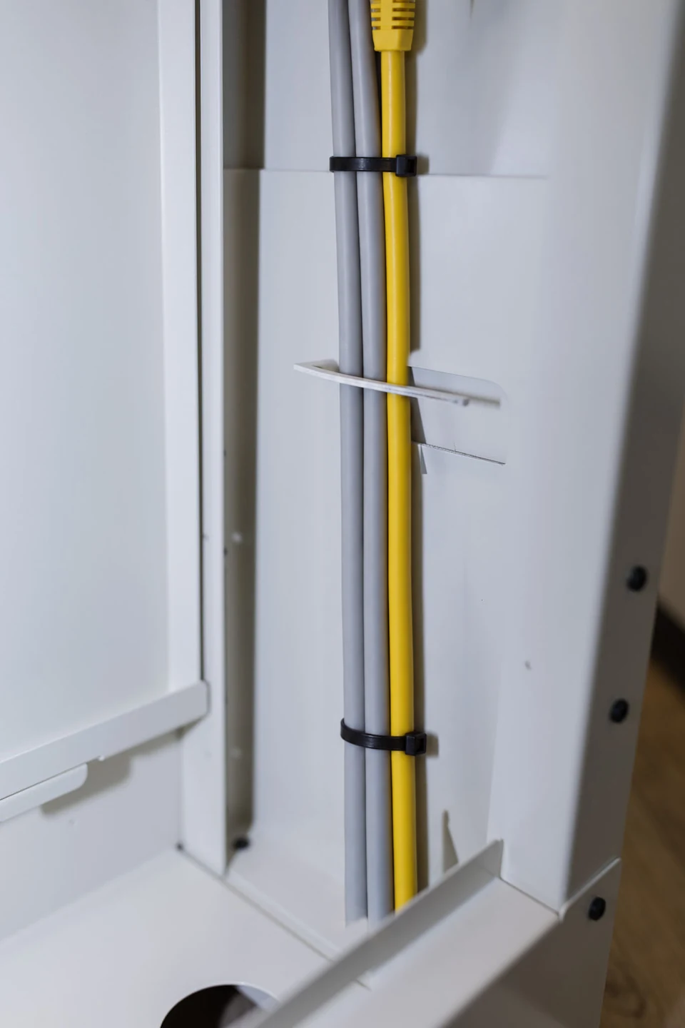 Im geöffneten Tischbein eines SMESK Tischs laufen zwei graue Kabel und ein gelbes Netzwerkkabel gerade nach unten, mit Kabelbindern gebündelt