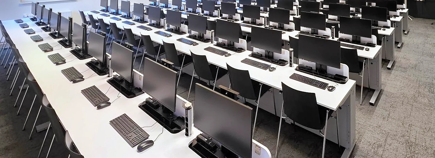 Großer Computerraum mit Reihen von SMESK Lift Tischen: an allen Plätzen stehen die Monitore ausgefahren, davor Tastatur und Maus