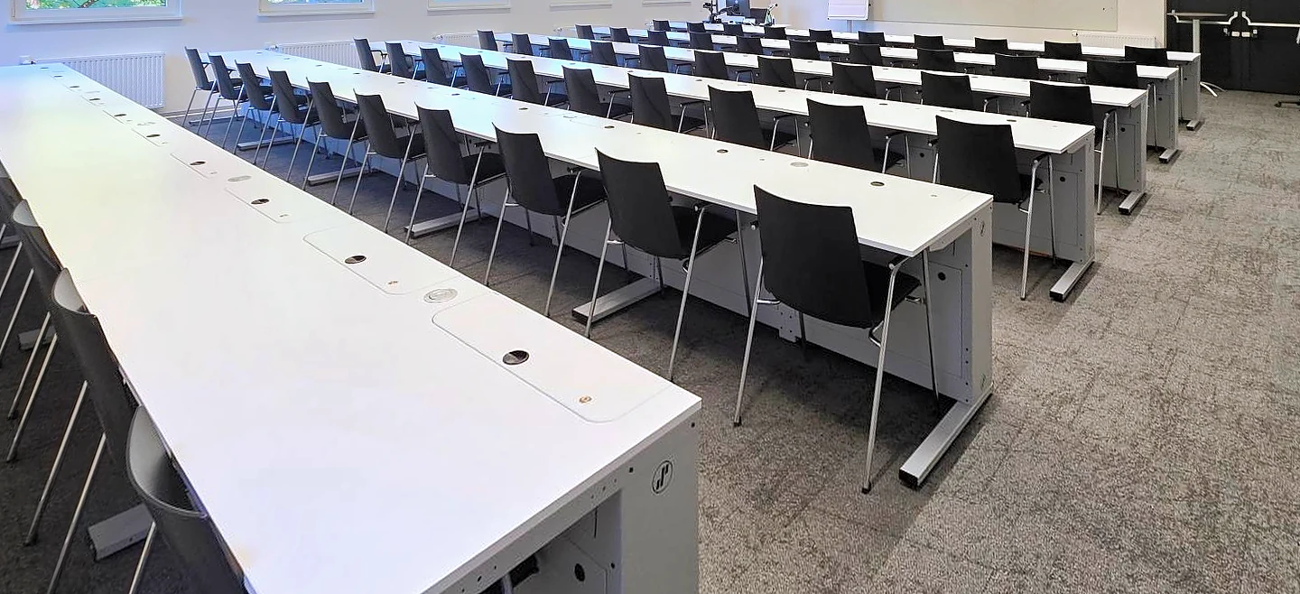 Unterrichtsraum mit Reihen von SMESK Lift Tischen: alle Monitore sind versenkt, die weißen Tischplatten sind frei