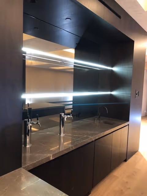 Modern bathroom vanity with a large mirror, LED strip lights, marble countertop, and two chrome faucets.
