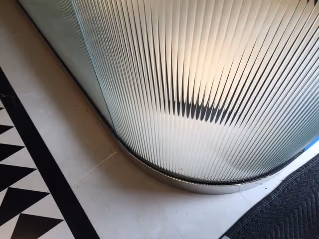 Curved ribbed glass wall panel with black and white triangular patterned floor on the left and a black textured rug on the right.