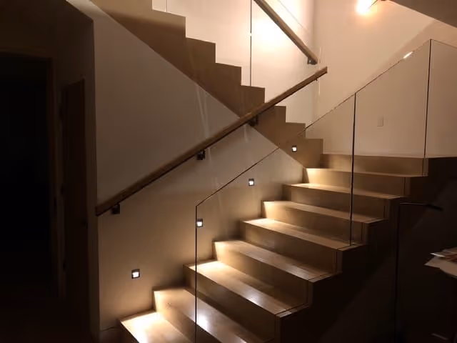 Modern indoor staircase with glass railing and built-in step lights illuminating each wooden step.