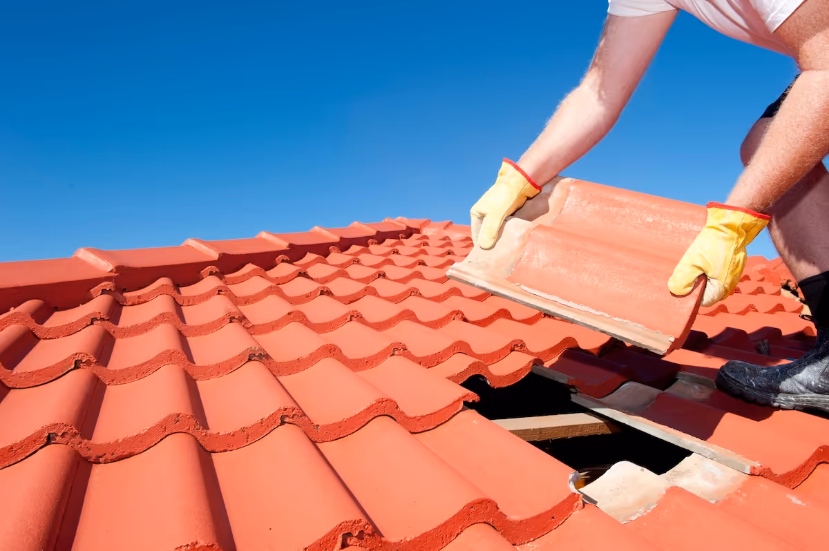 Roofer installing red clay tile shingles on a residential roof