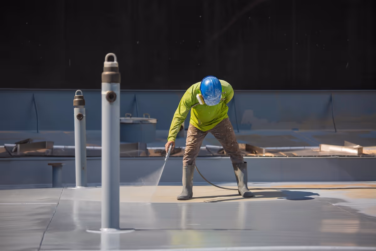Worker applying silicone roof coating around penetrations on a flat roof